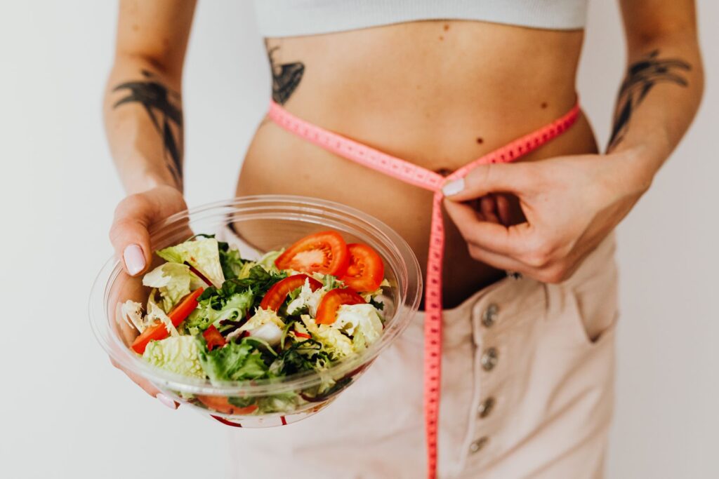 Femme mesurant son tour de taille avec un bol de salade, prise de poids à la ménopause